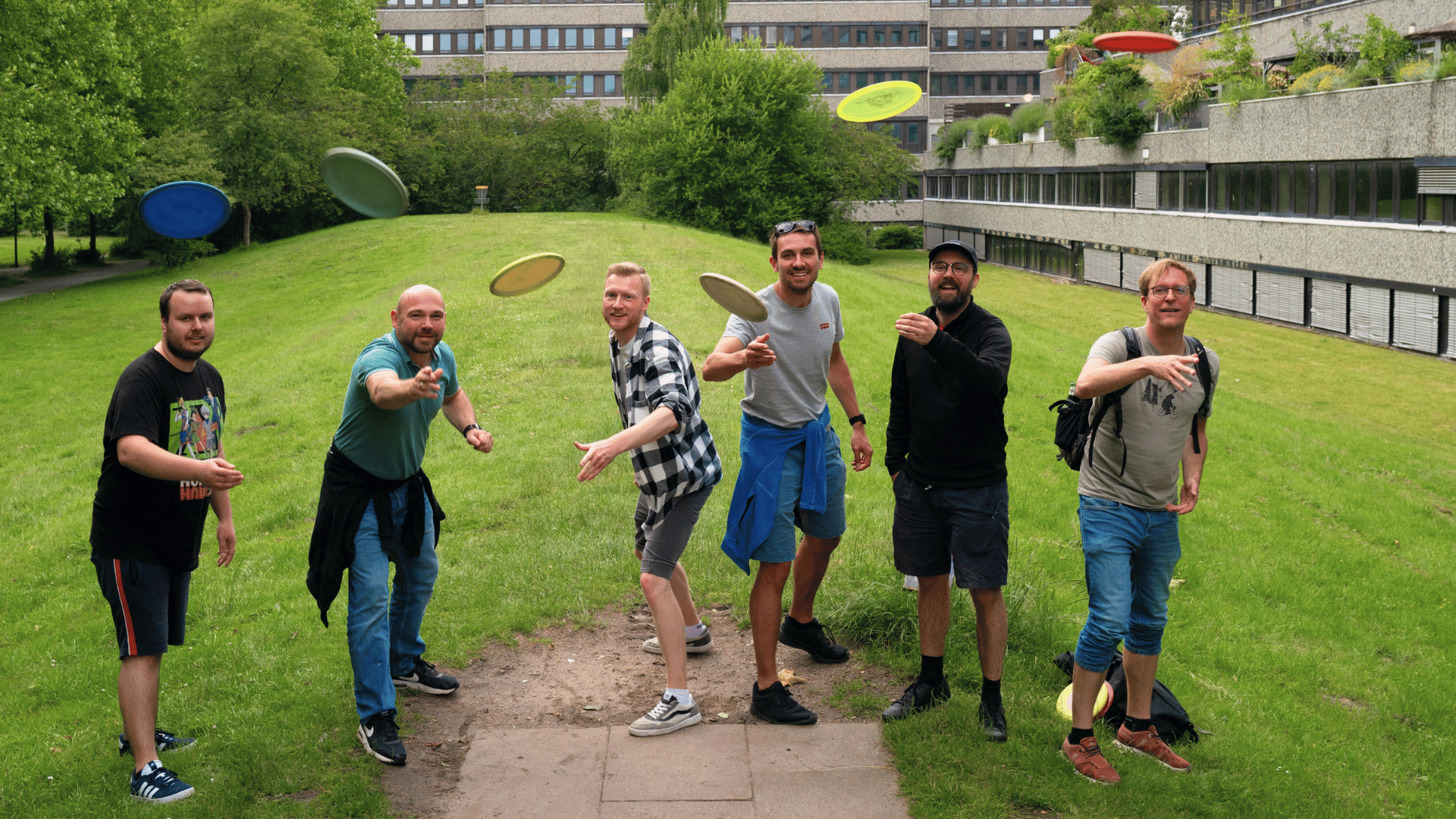 Einige Ubilabs-Mitarbeitende stehen auf einer Wiese und werfen Discs vom Disc-Golf Richtung Kamera.